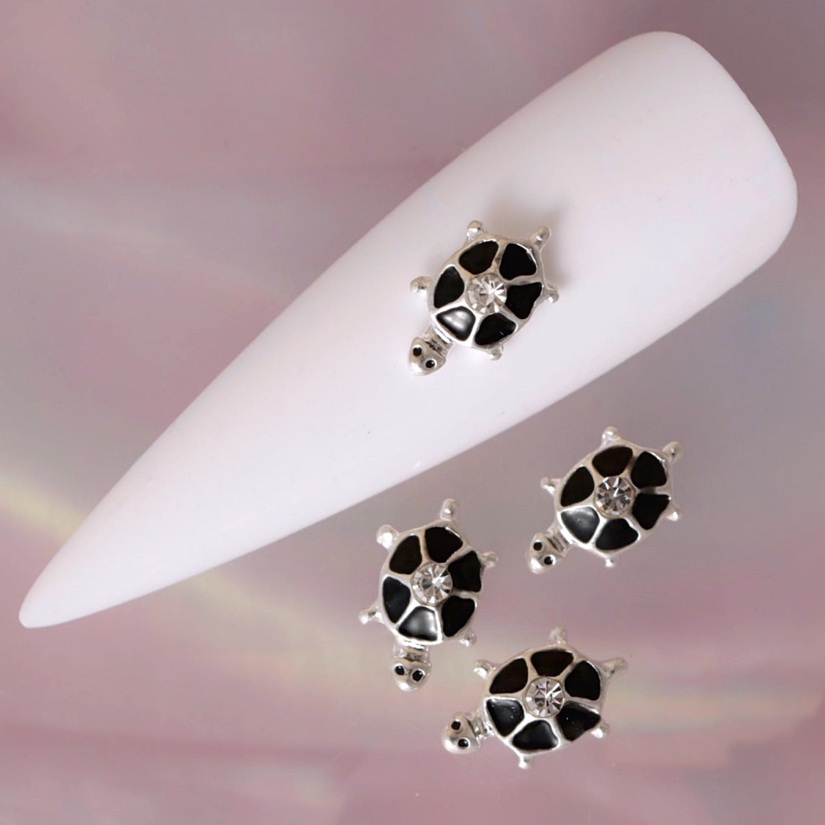 Silver turtle nail charm featuring a patterned black shell, small raised limbs and a clear rhinestone in the centre. This elegant animal-inspired decoration is ideal for summer manicures, beach nail art, ocean-themed designs and creative accent nails.