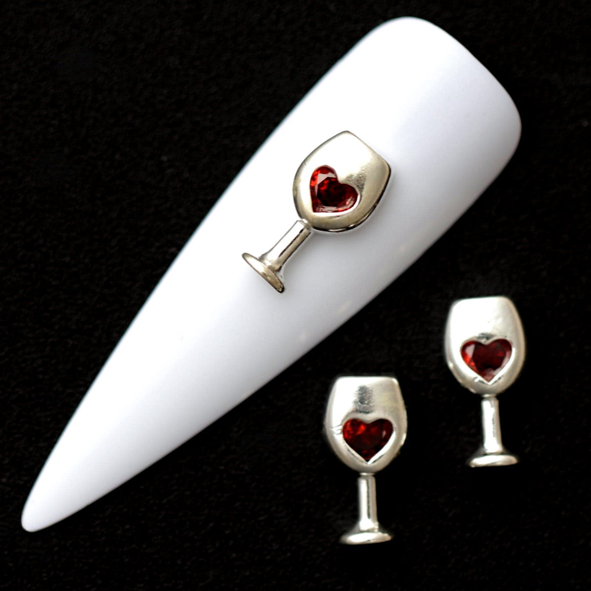 Silver 12×6 mm wine glass nail charms with red heart-shaped CZ stones displayed on a white nail tip against a black background