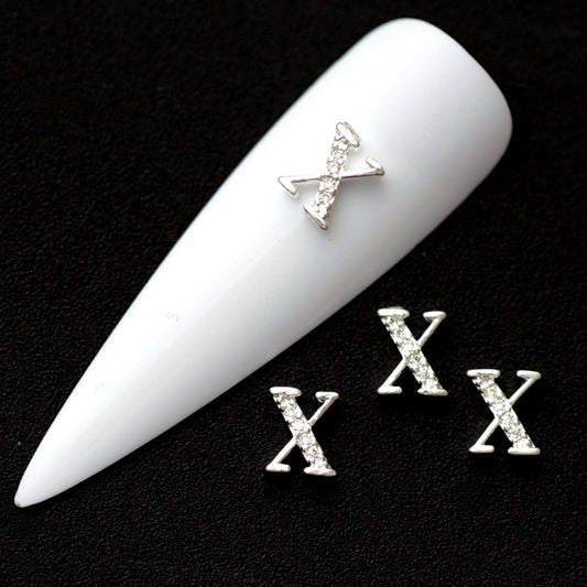Silver X letter nail charms paved with crystal cubic zirconia on a white nail tip against a black background