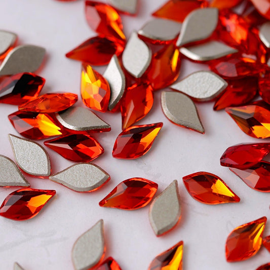 A Swarovski 2205 Flame flatback crystal in Fireopal, measuring 7.5 mm. The flame-shaped crystal features a pointed upper section, a fuller lower body and precision-cut facets. Its fiery colour transitions from luminous yellow and golden amber to warm orange, bright red and deep ruby tones. Ideal for statement nail art, flame designs, autumn manicures and luxury crystal embellishment.