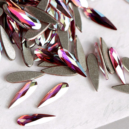A pile of teardrop-shaped Swarovski 2304 Light Rose AB flatback rhinestones with a metallic silver backing, showing iridescent pink, purple, and blue reflections on a light gray background.
