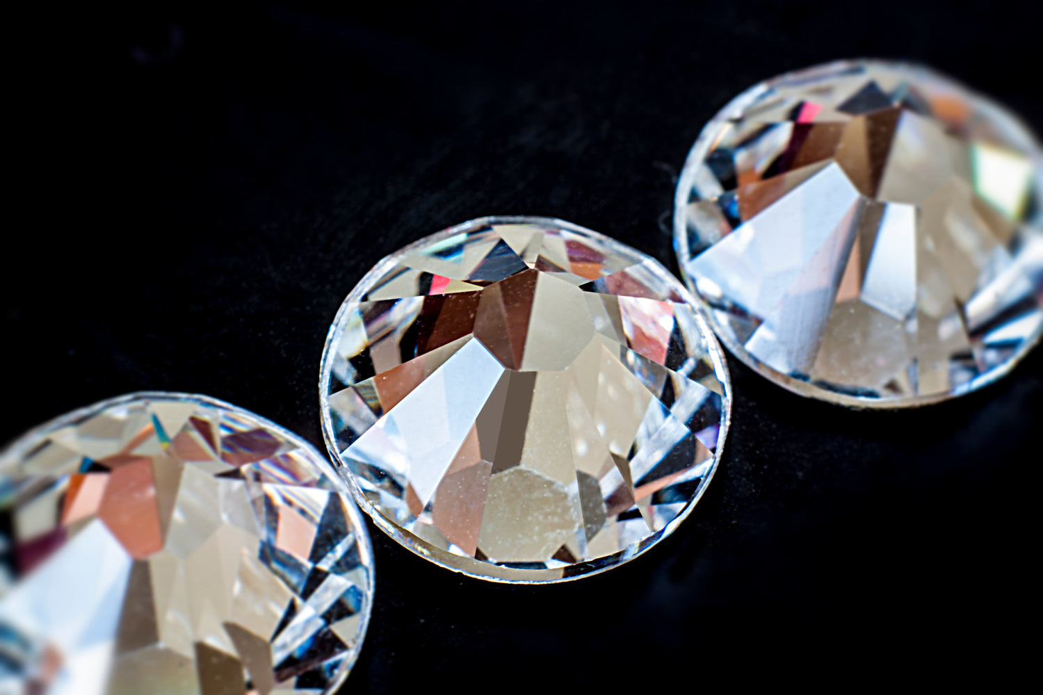 Close-up of three clear Swarovski flatback round crystal rhinestones on a black background, showcasing their brilliant sparkle and precision cut for nail art and crafts