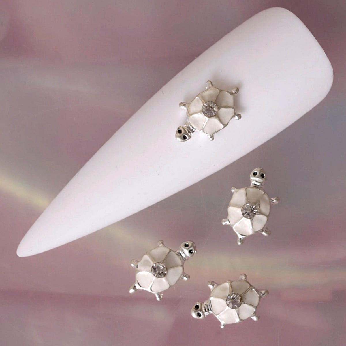 White turtle nail charm featuring a segmented white shell, polished silver-tone details, small raised limbs and a clear rhinestone in the centre. This elegant animal-inspired decoration is ideal for summer manicures, beach nail art, ocean-themed designs, bridal manicures and delicate accent nails.